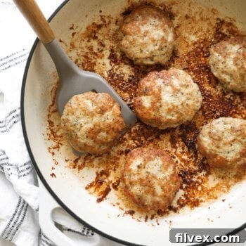 Overhead image of a cast iron skillet with chicken sausage patties in it. A spatula lifting one patty out of the pan.