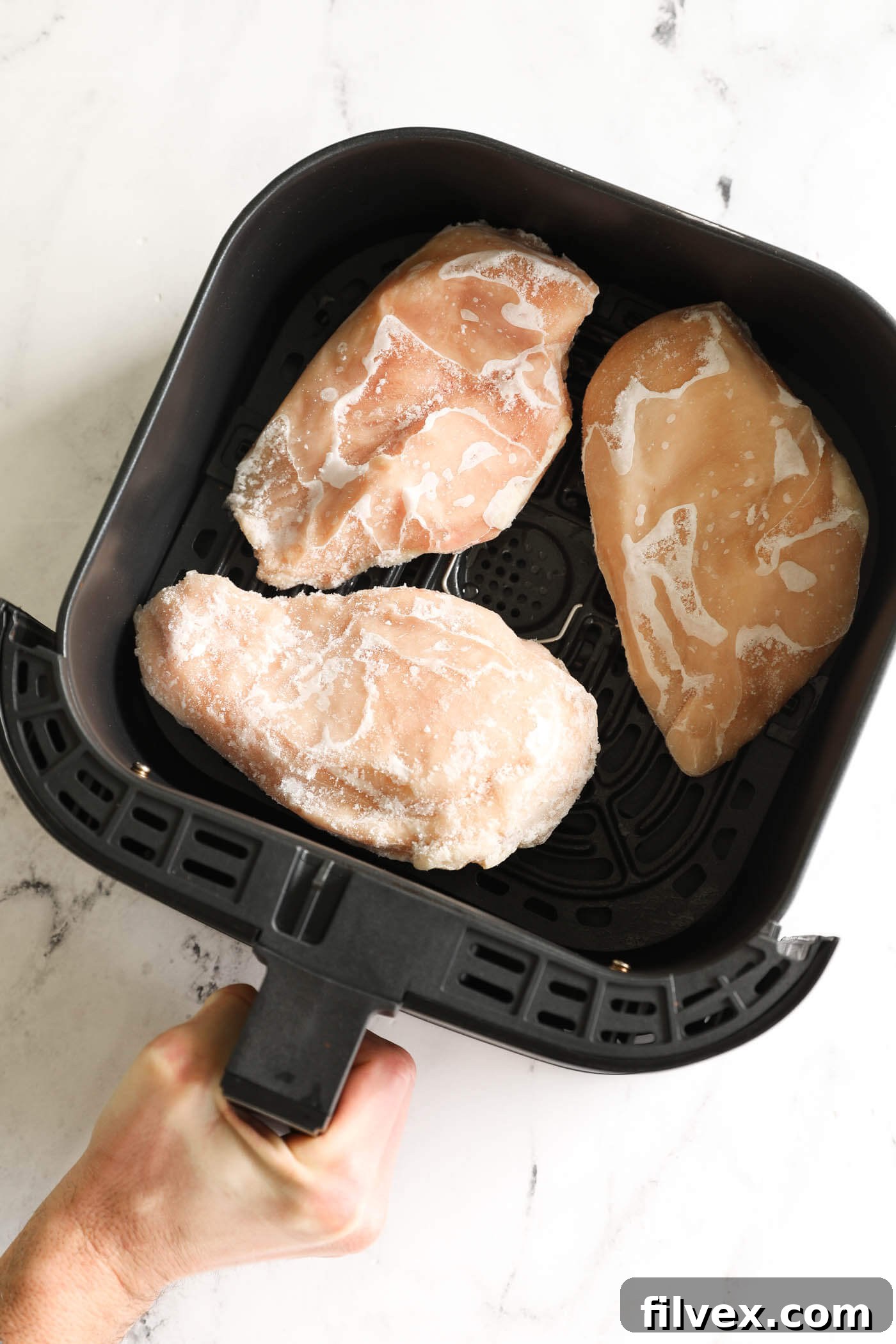 Frozen chicken breasts being placed in an air fryer basket