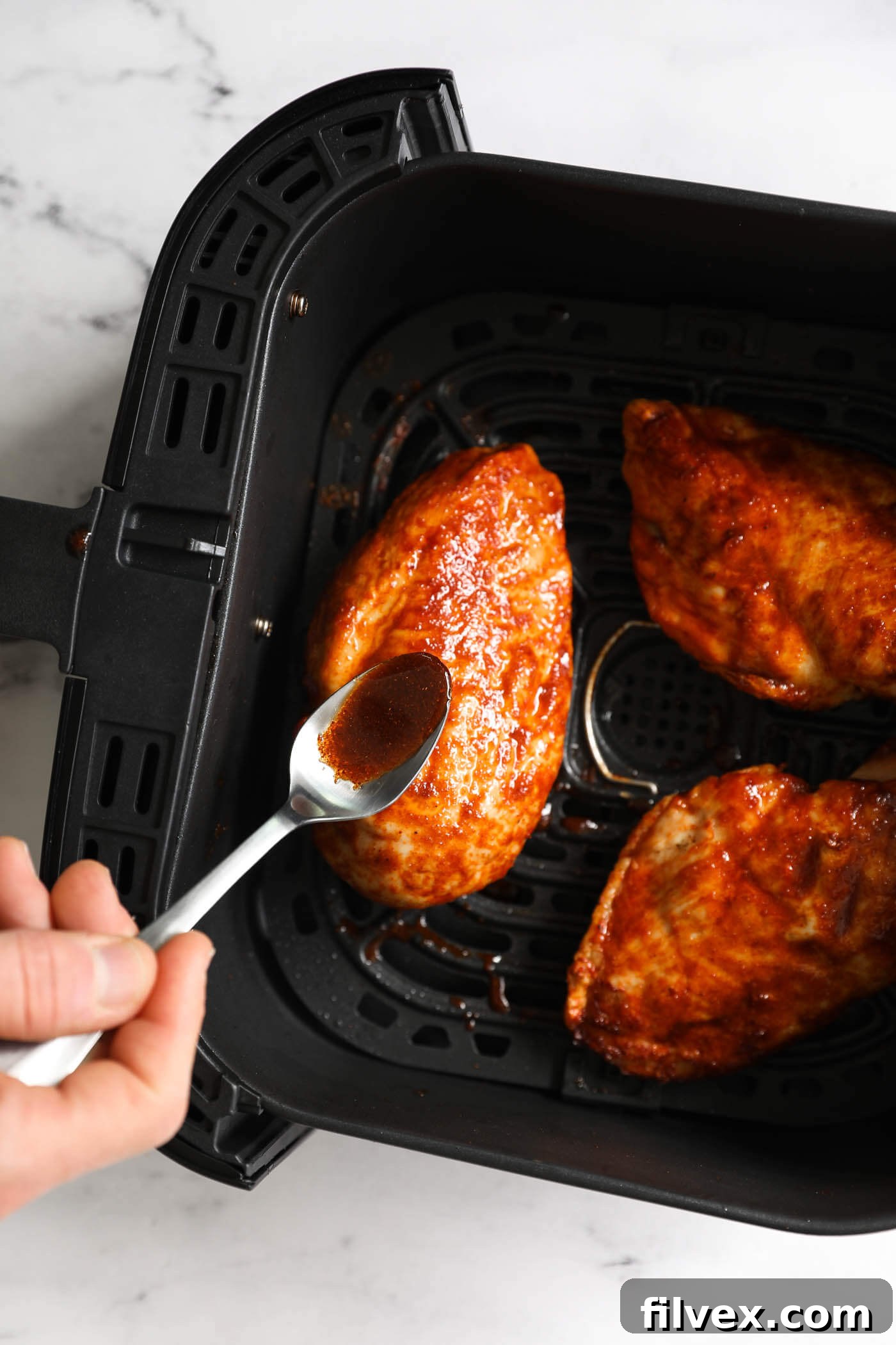 Brushing sauce onto cooked chicken breasts in the air fryer