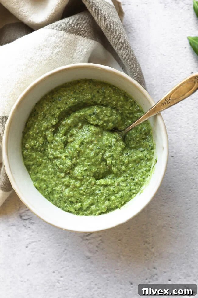 Bowl of dairy-free and nut-free pesto in a bowl with a spoon, highlighting its creamy texture.