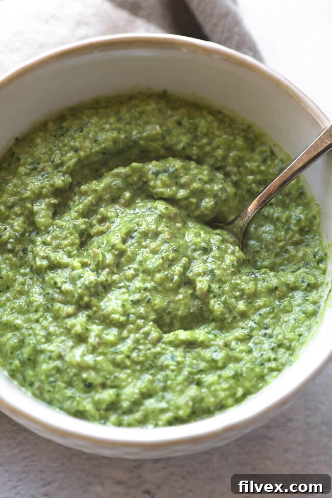 Overhead close-up of vibrant dairy-free and nut-free pesto in a bowl with a spoon, ready to be served.