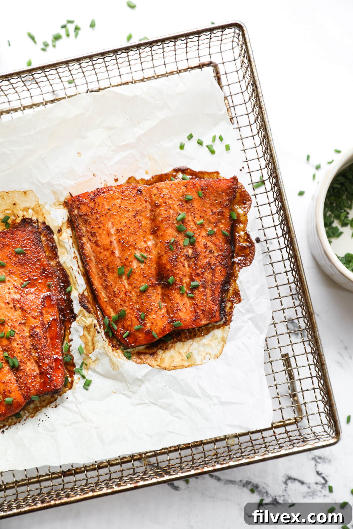 Overhead image of air fryer salmon on tray with chopped chives sprinkled on top.