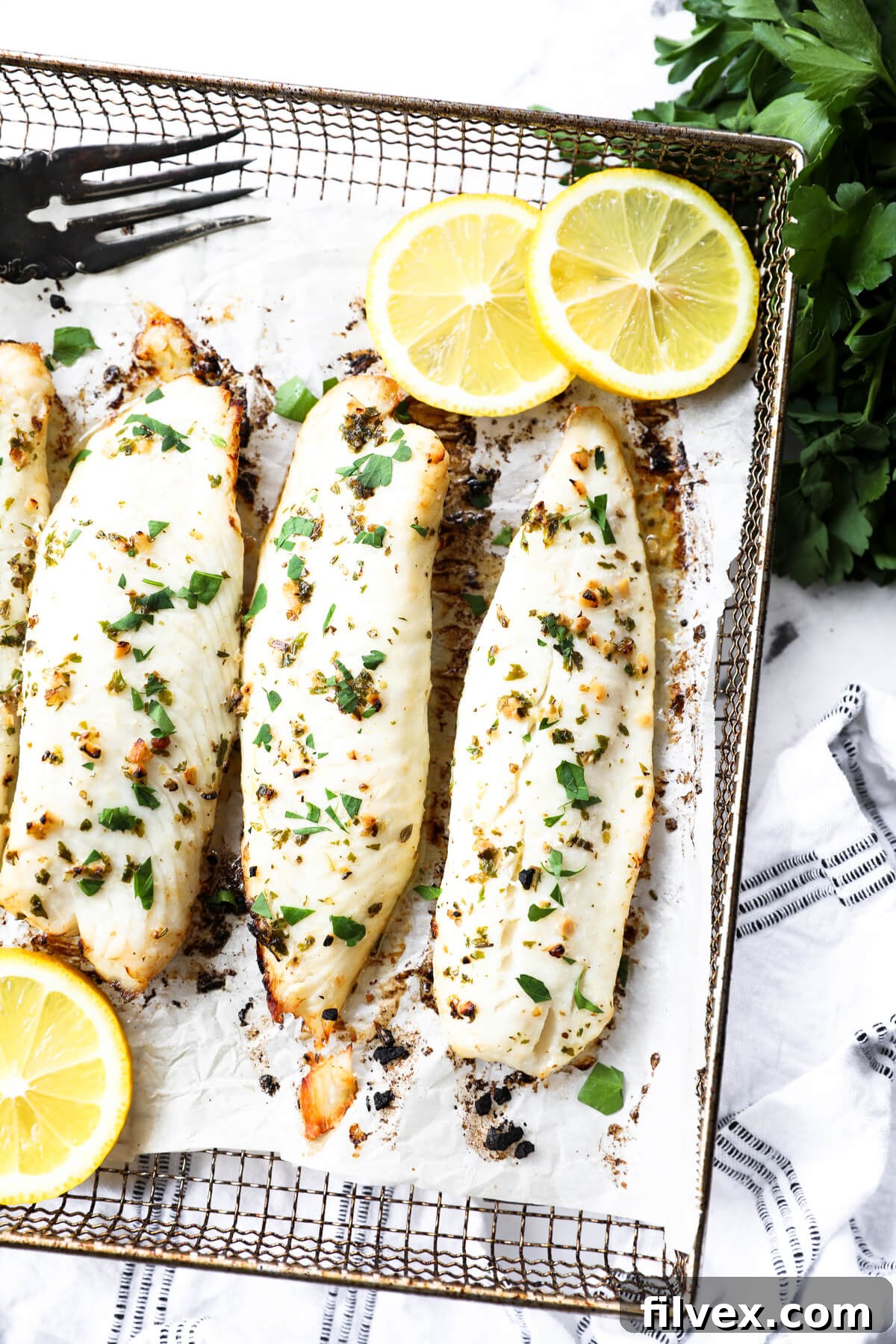 Close up of three pieces of air fried tilapia in a horizontal line with fresh parsley and lemon slices to garnish.