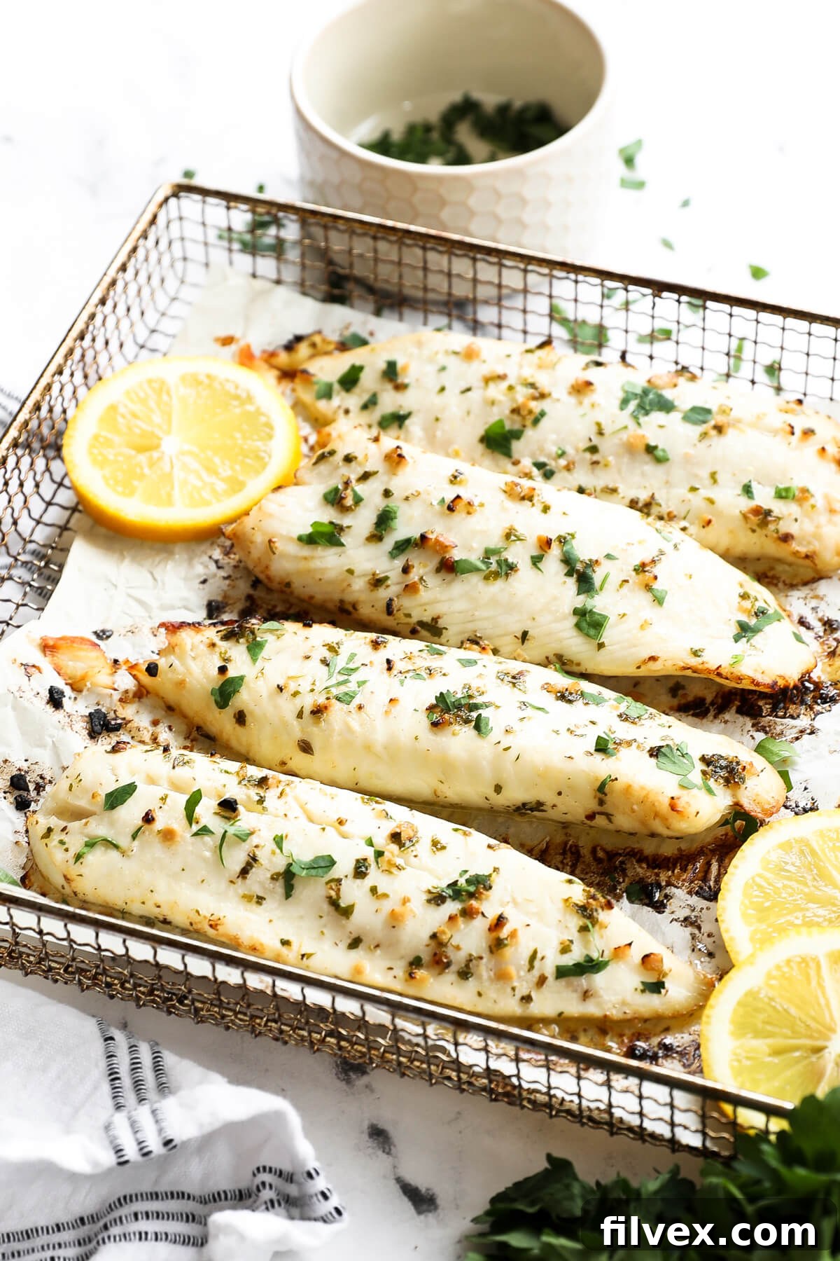 Angled image of air fryer tilapia in cooking basket with lemon slices and parsley garnish.