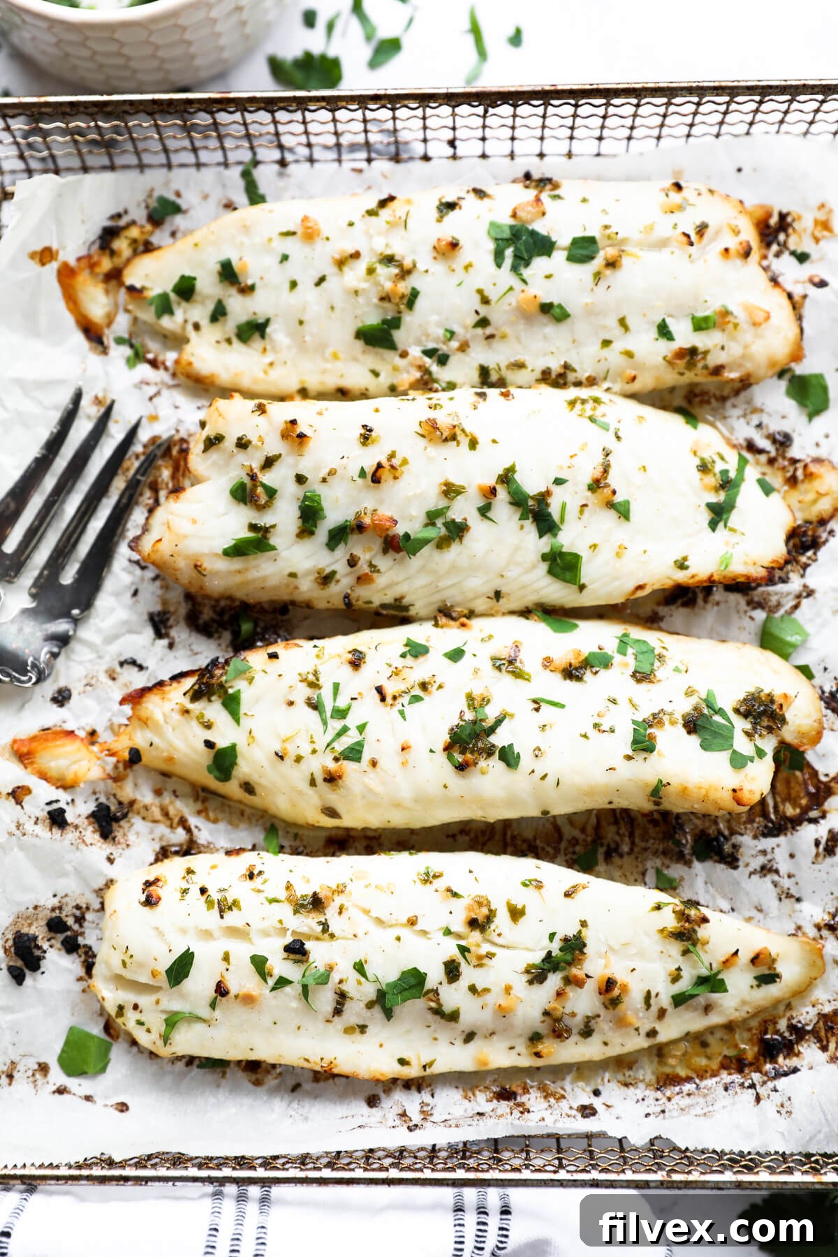 Overhead close up image of four pieces of tilapia lined up in a row. Fresh chopped parsley sprinkled on top.