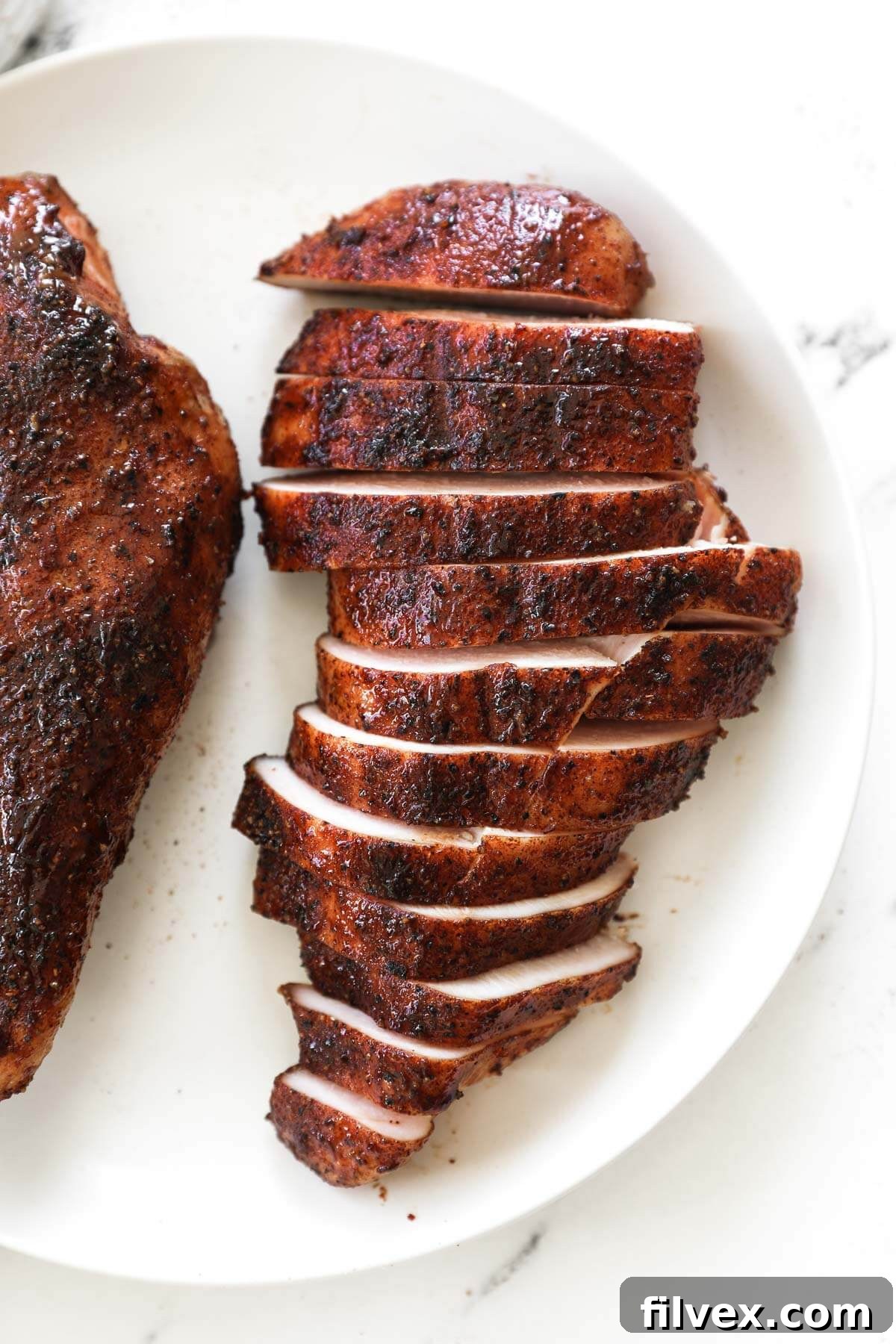 Overhead image of smoked chicken breast cut into strips on a plate, garnished with fresh herbs.