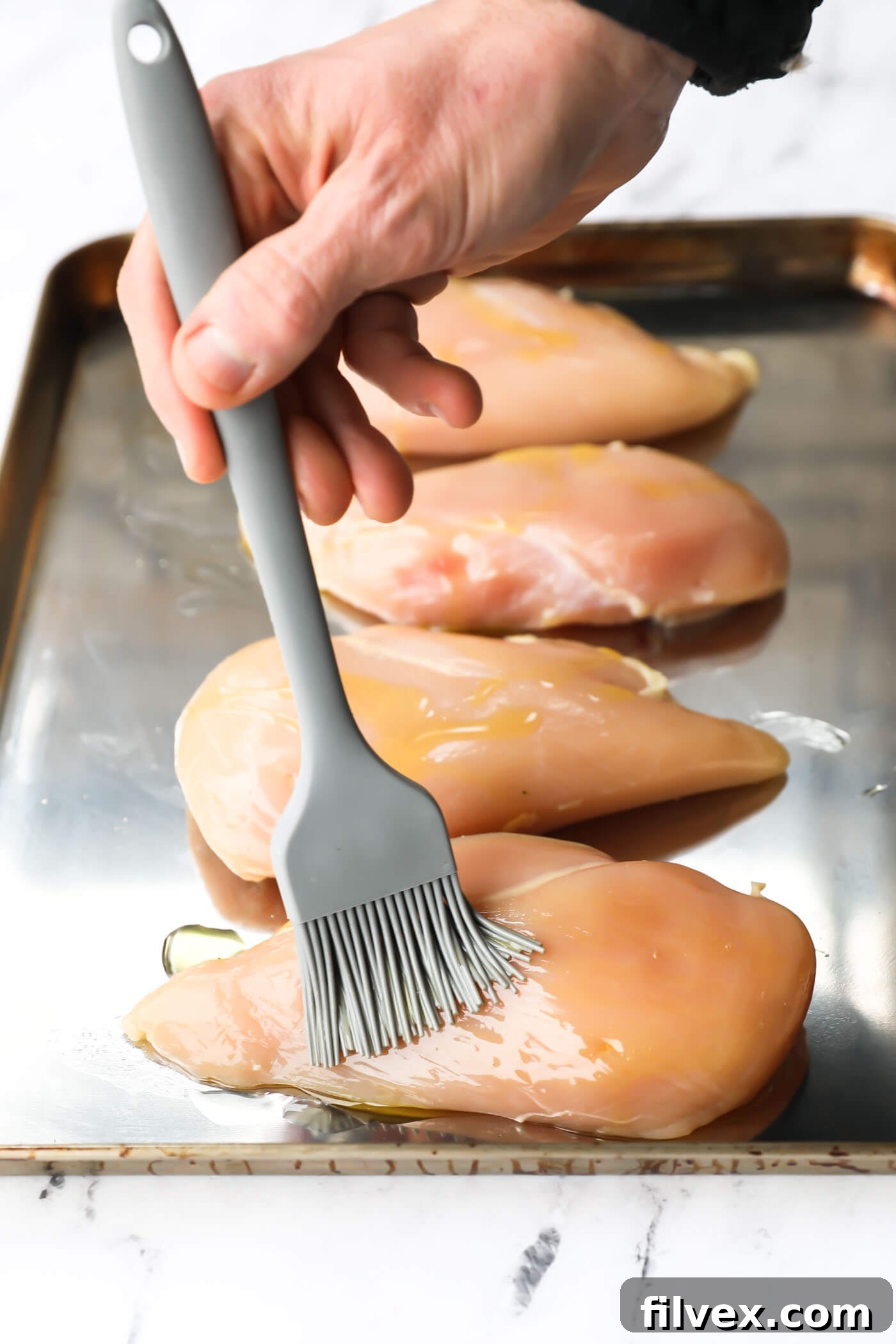 Raw chicken breast being drizzled with avocado oil.