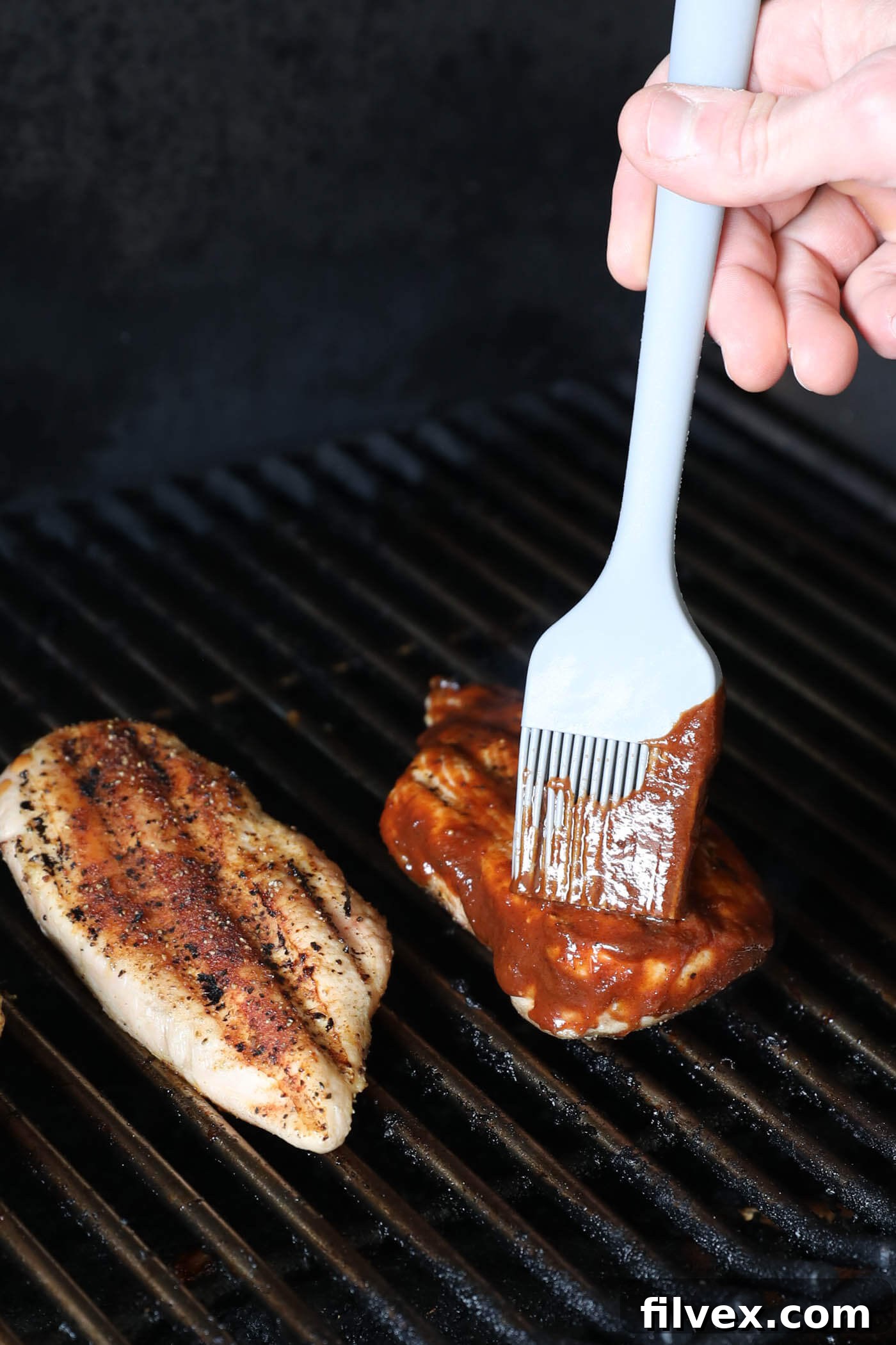 Smoked chicken breast being brushed with BBQ sauce on the grill.