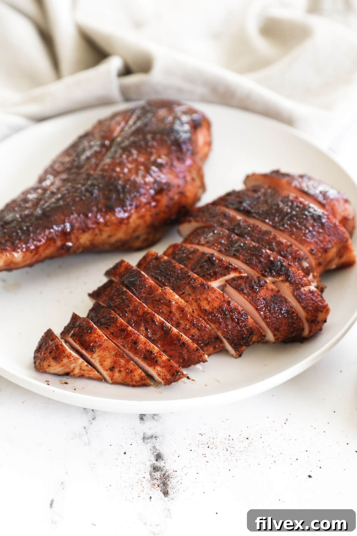 Angled image of two pieces of smoked chicken breast on a plate. The closest piece is expertly sliced into strips, revealing its juicy interior.