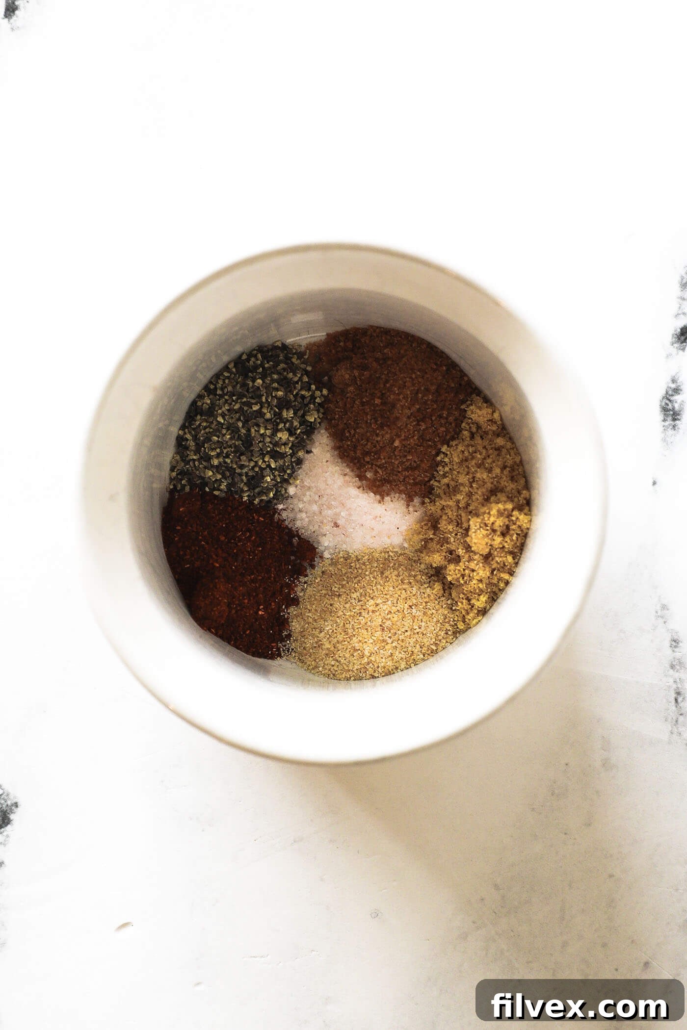 A small jar containing a custom seasoning mix, ready to be applied to pork chops.