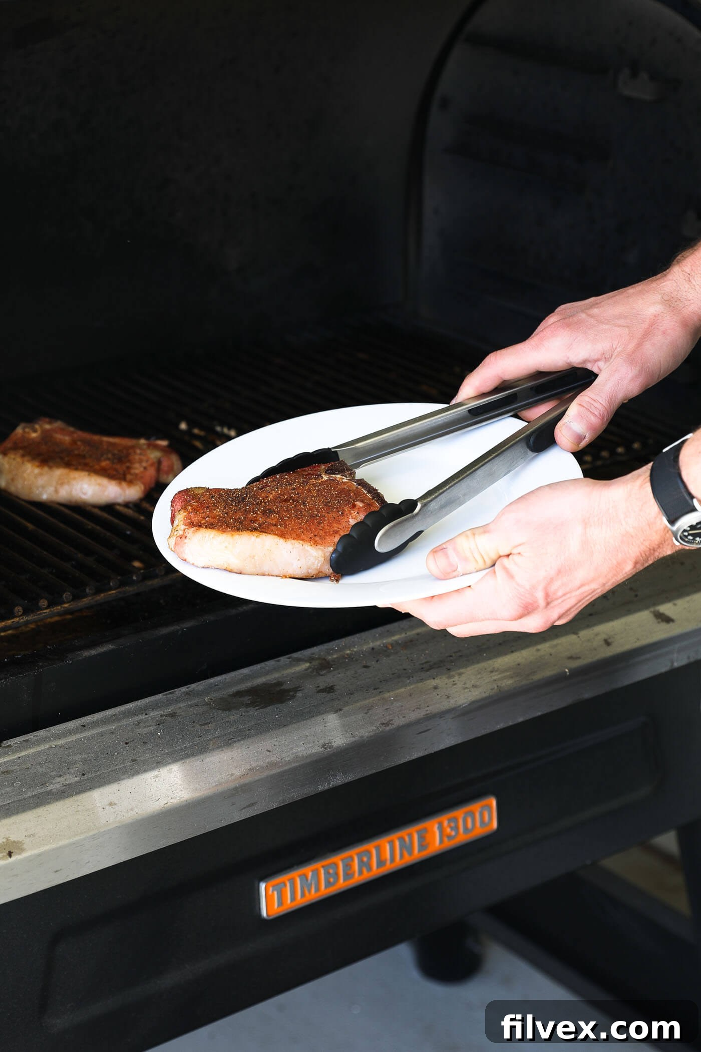 Pork chops removed from the smoker and resting on a platter, while the grill preheats to a higher temperature for searing.