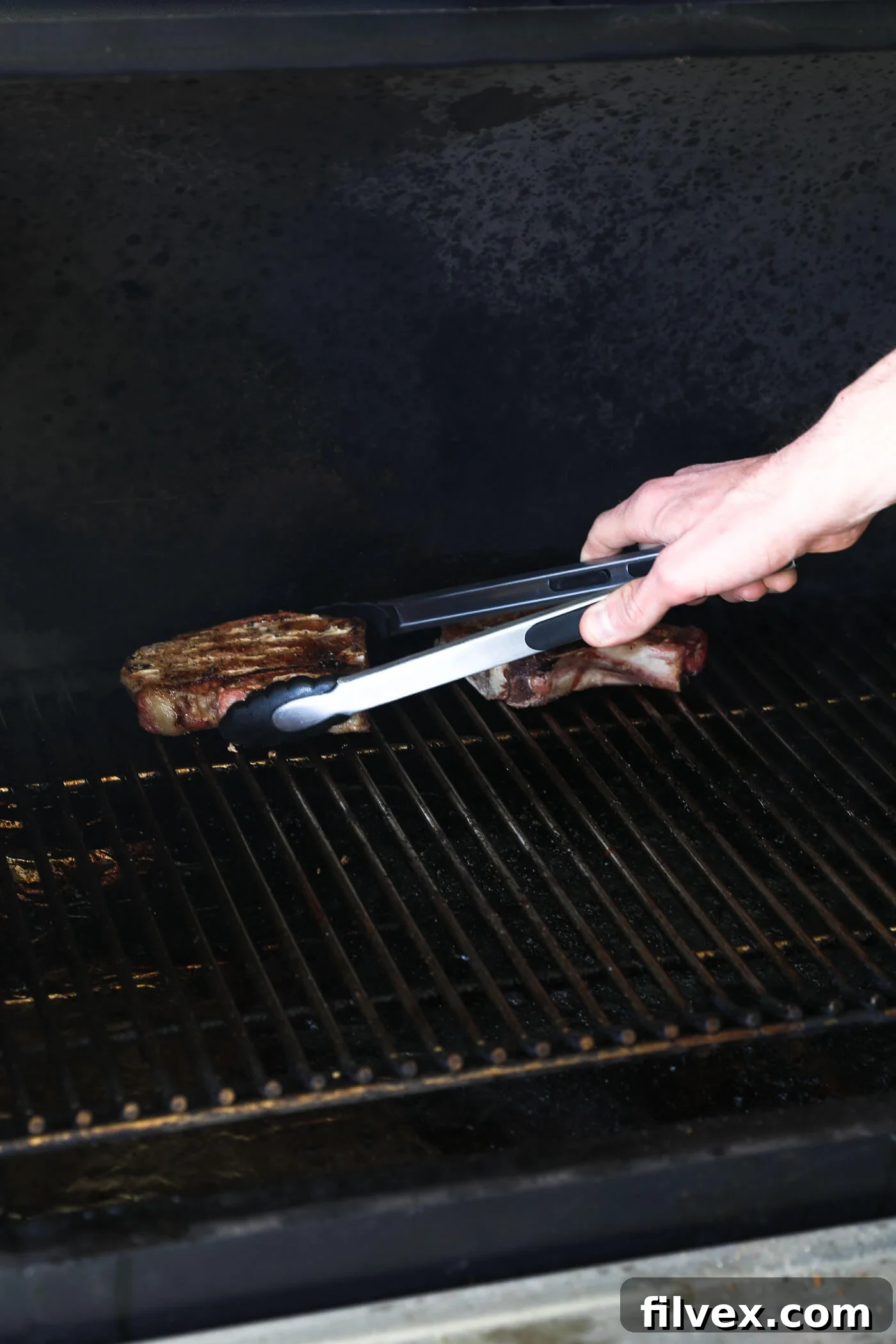 Smoked pork chops being placed back onto the blazing hot grill grates for a quick reverse sear.
