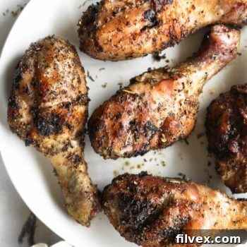 Close up overhead image of smoked chicken drumsticks on a white plate with seasoning sprinkled around