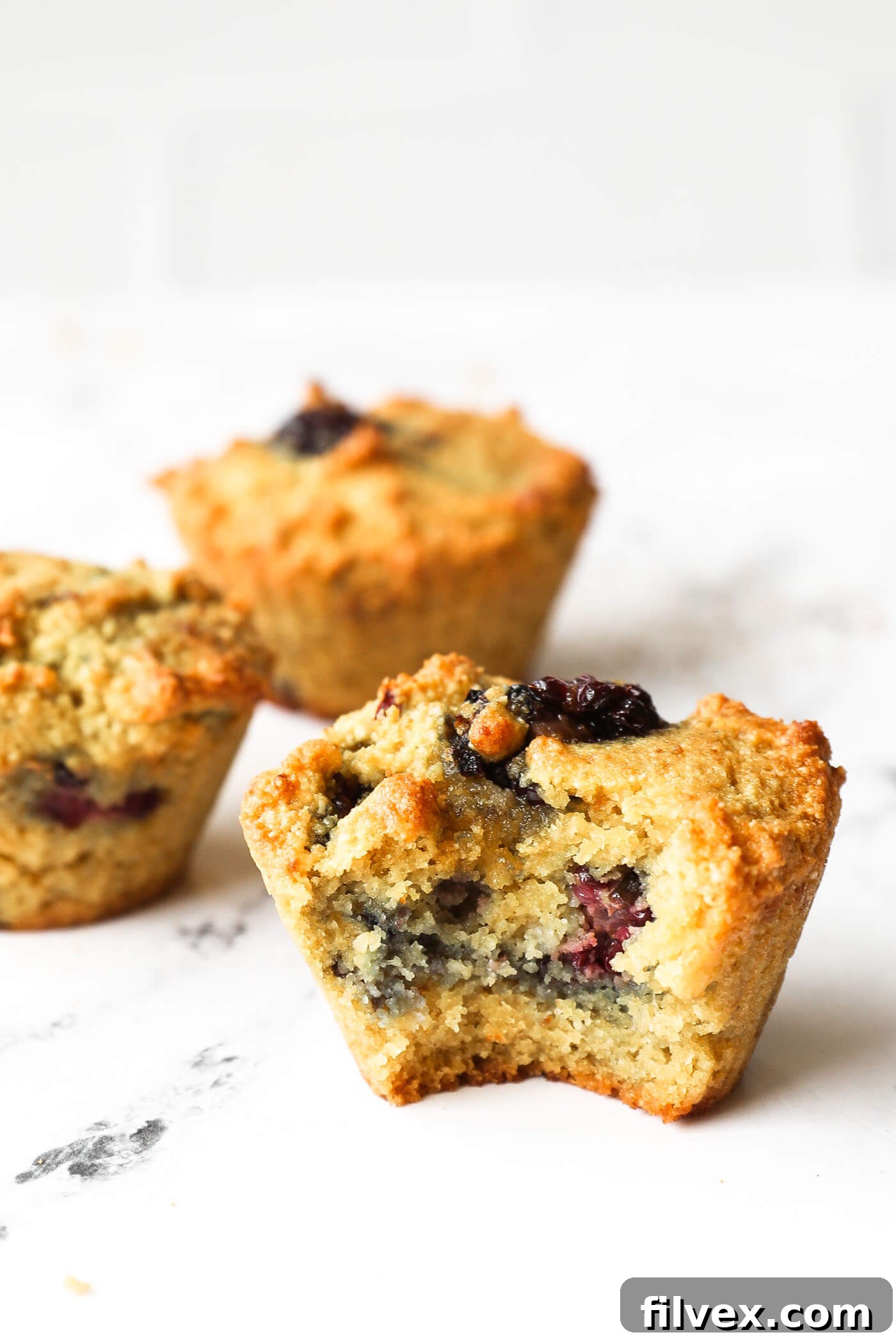 Image of three gluten free blackberry muffins on table. One muffin has a bite taken out of it.