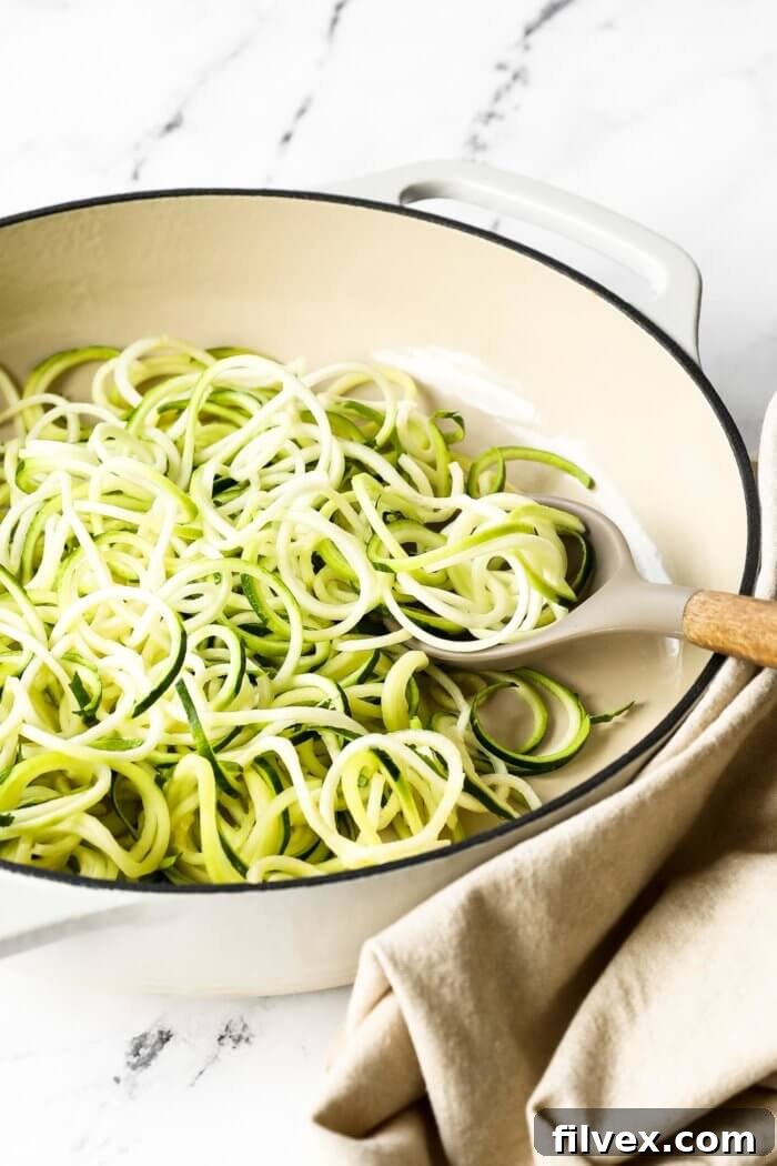Angled image of zucchini noodles in a skillet with a serving spoon.