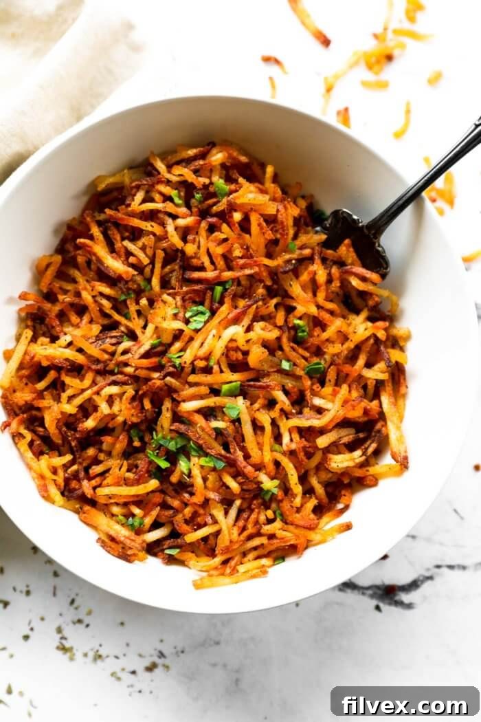 Pile of golden-brown crispy air fryer hash browns on a plate next to a runny fried egg and fresh herbs
