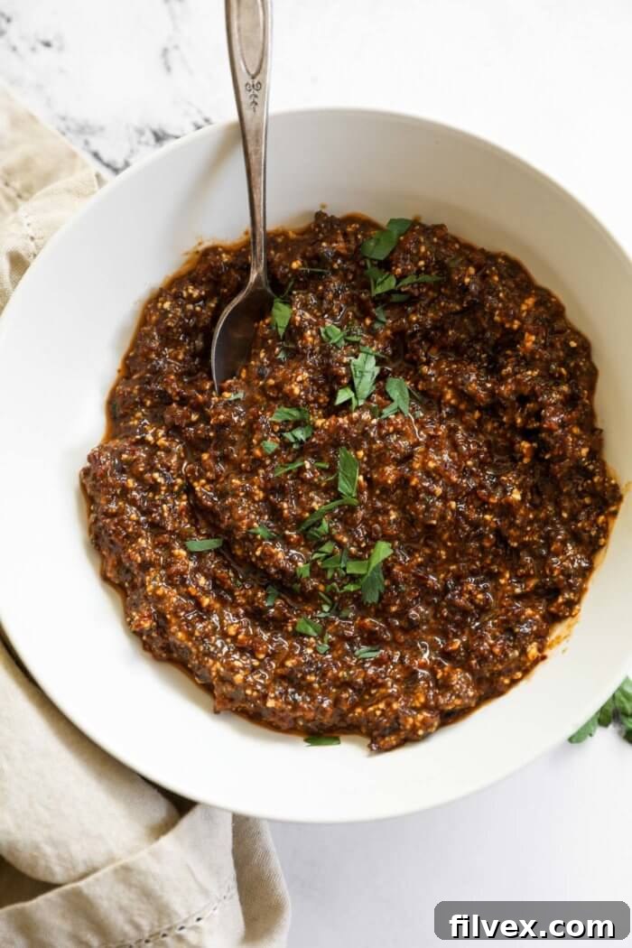 Overhead shot of sun-dried tomato pesto in a white bowl with a spoon and parsley garnish