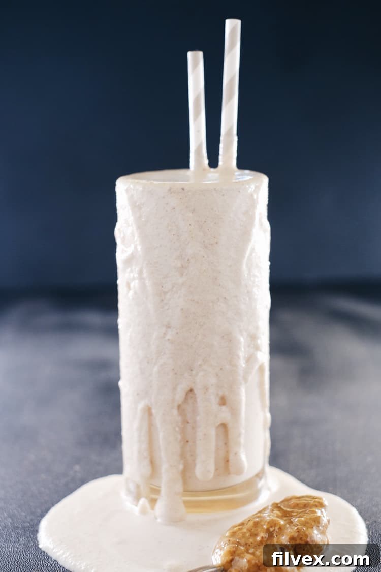 A tall glass of creamy banana almond butter smoothie, garnished with a sprinkle of cinnamon, sitting on a rustic wooden surface. It's a healthy, easy-to-make smoothie that's Paleo, Gluten-Free, Dairy-Free, and Refined Sugar-Free.