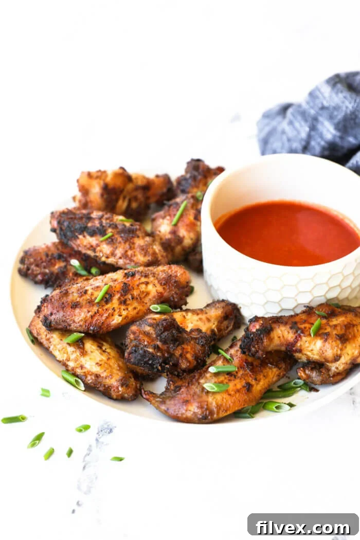 Angled image of crispy chicken wings piled on a plate with buffalo sauce in a ramekin on the side.