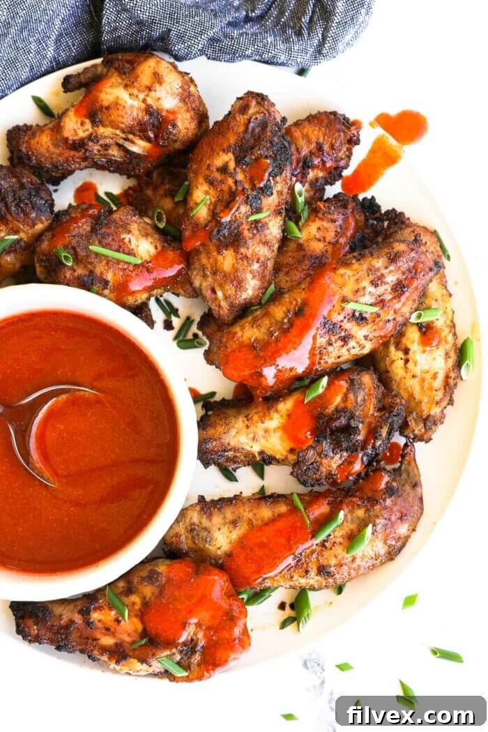 Close up overhead image of chicken wings on a plate with buffalo sauce drizzled on top.