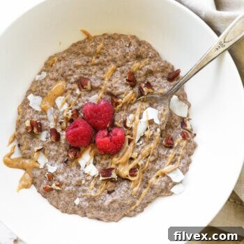 Overhead image of a bowl with chia pudding and toppings including peanut butter, coconut flakes, chopped pecans and raspberries.