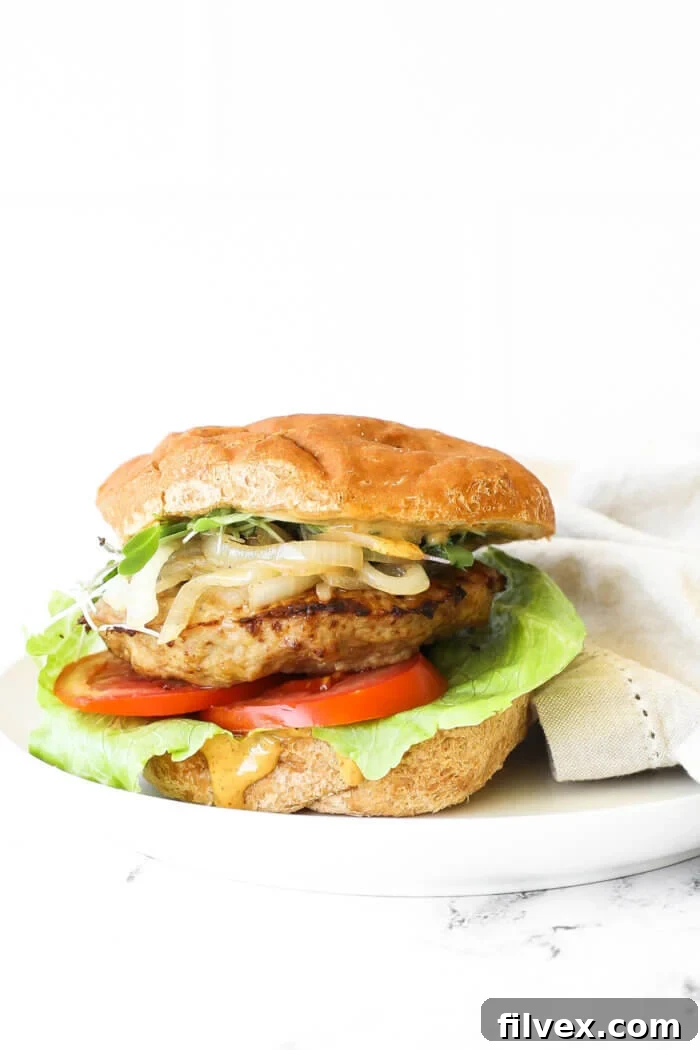 A perfectly loaded turkey burger on a gluten-free bun, showcasing fresh lettuce, ripe tomato, a thick turkey patty, sweet caramelized onions, and vibrant microgreens, all drizzled with chipotle aioli.