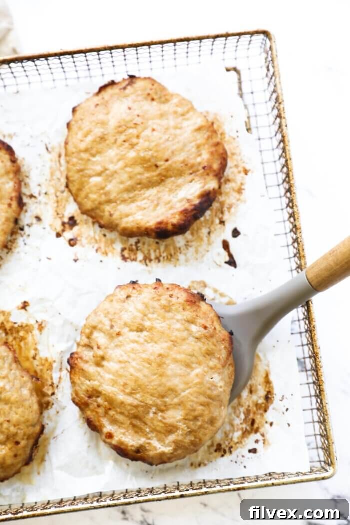 Turkey burger patties cooking inside an air fryer basket, with one patty being carefully lifted by a spatula to check for doneness.