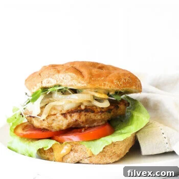 Image of a loaded turkey burger on a gluten free bun. Toppings include chipotle aioli, lettuce, tomato, turkey patty, caramelized onions and microgreens.