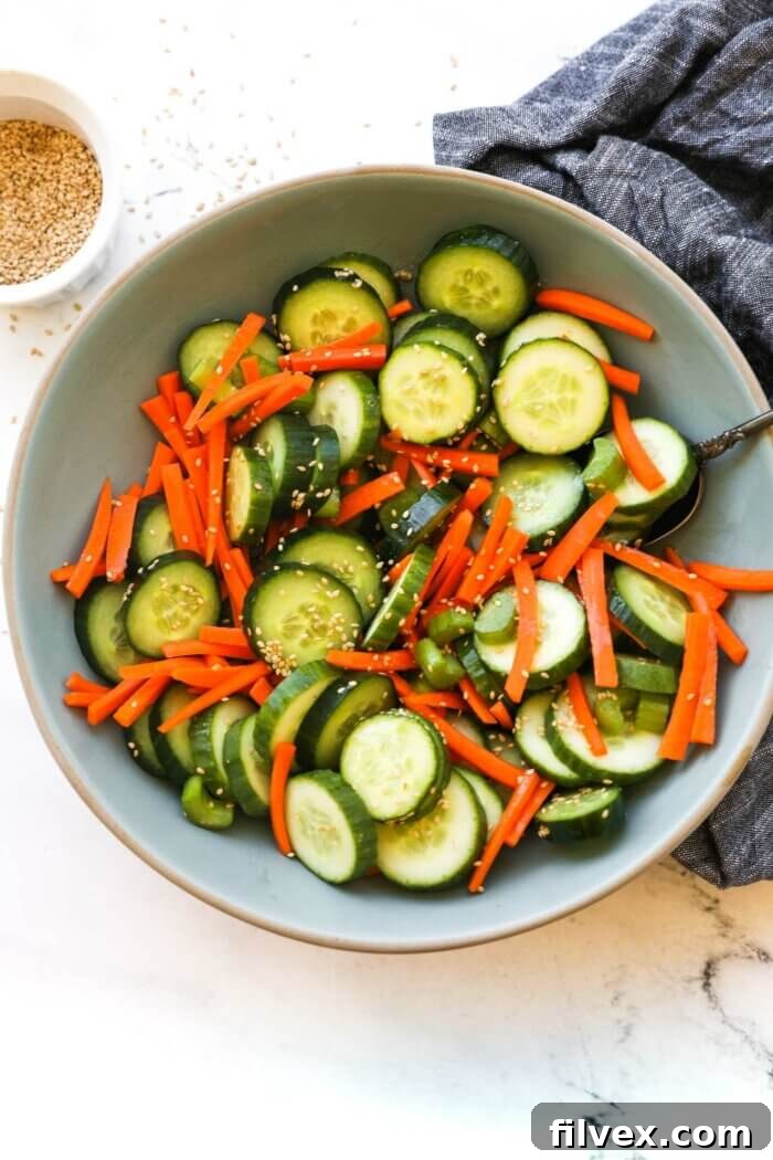 Overhead image of a bowl full of cucumber, carrots and celery with a sesame sauce and sesame seeds. Ingredients are all mixed up. 
