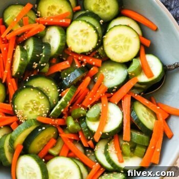 Close up overhead image of a bowl full of cucumber, carrots and celery with a sesame sauce and sesame seeds. Ingredients are all mixed up.