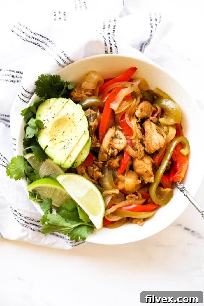 A bowl full of chicken fajitas with sliced avocado, lime wedges and fresh cilantro, ready to be served.