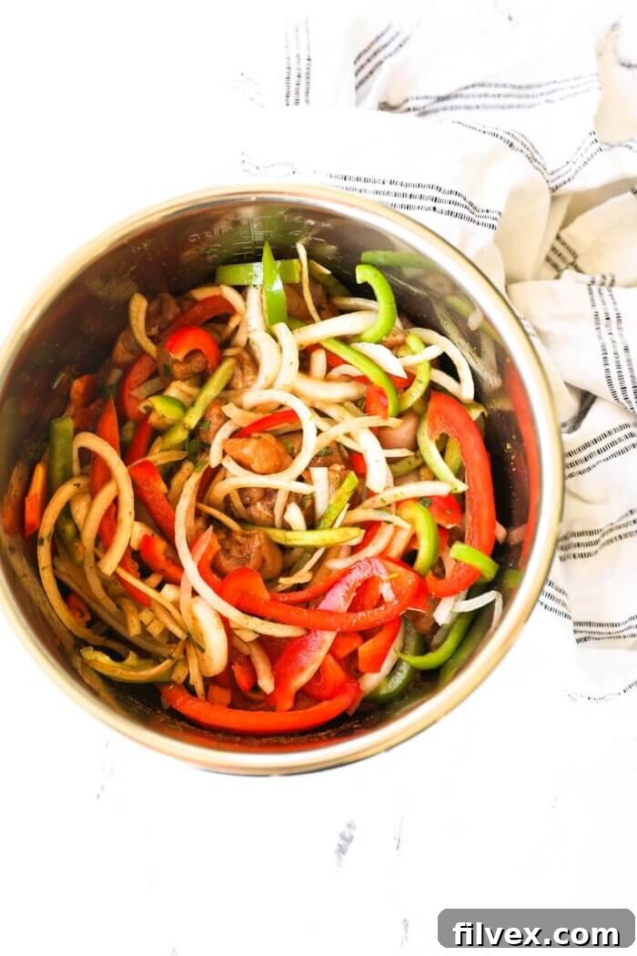 Overhead shot of an Instant Pot before cooking, filled with cut-up pieces of chicken, sliced red and green bell peppers, onion, and a flavorful marinade sauce, ready to be pressure cooked.