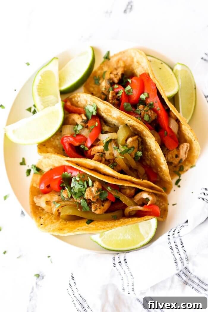 Overhead image of 3 taco shells filled with chicken fajitas. Topped with fresh chopped cilantro and lime wedges holding the tacos up, showcasing a delicious serving suggestion.