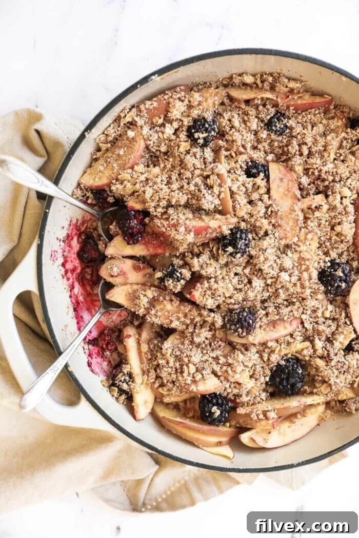 A rustic cast iron skillet filled with a freshly baked apple and blackberry crumble, topped with a golden, crumbly crust. Steam is gently rising, indicating its warmth.
