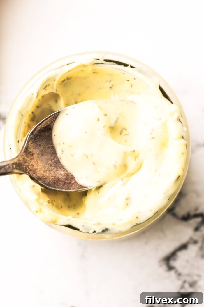 Overhead image of a spoonful of creamy, homemade keto tartar sauce being lifted out of a rustic glass jar, ready to be served.