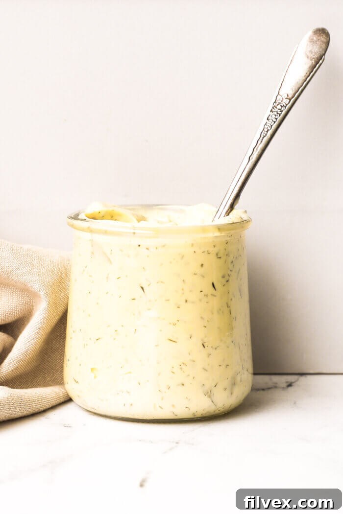 Straight on shot of a small jar filled to the top with homemade tartar sauce. A spoon is dug into the jar, poised to serve.