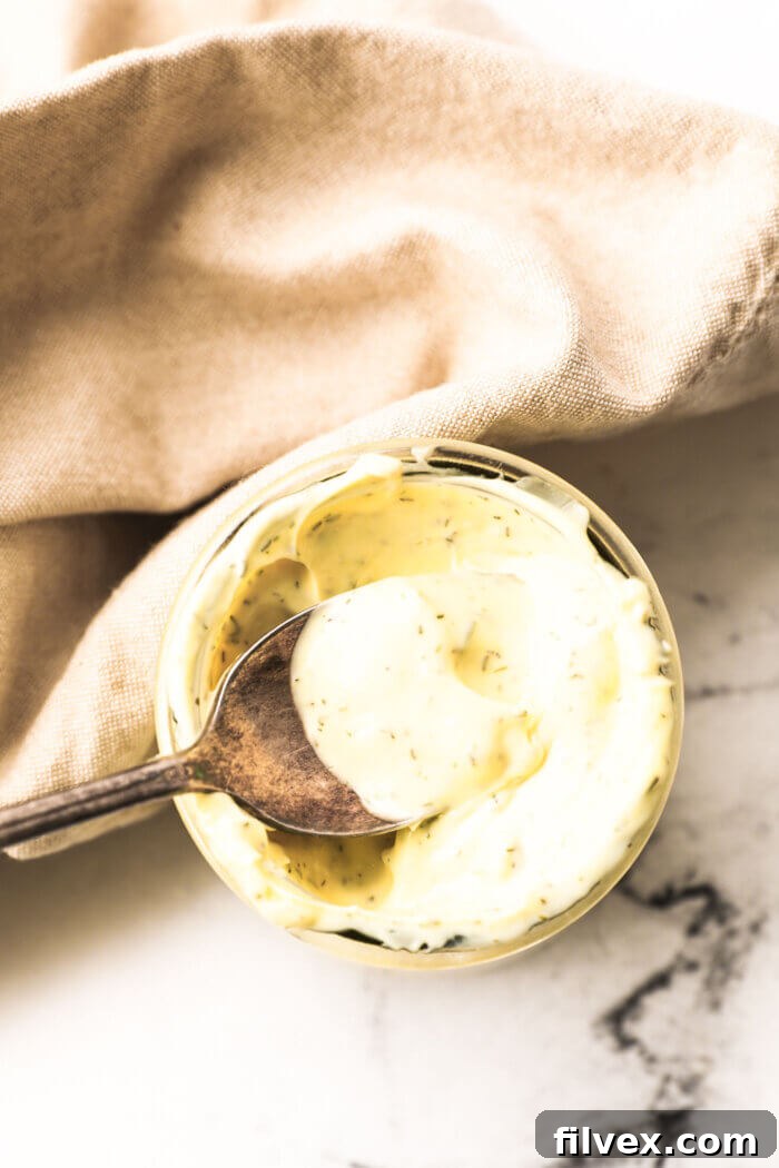 Overhead image of a spoonful of creamy homemade keto tartar sauce being lifted out of the jar, highlighting its rich texture.