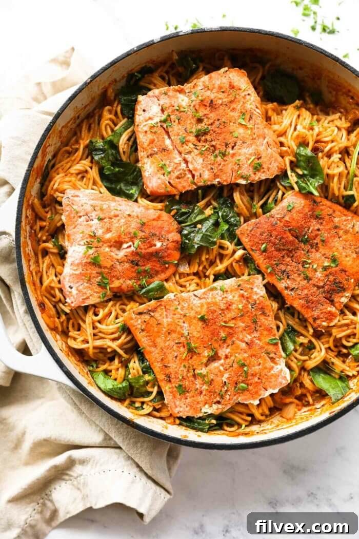 Close up overhead image of a skillet filled with creamy cajun salmon pasta and four cajun salmon filets.