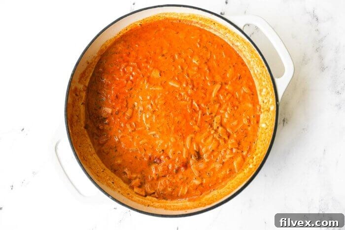 Orange/red creamy cajun salmon pasta sauce simmering in a skillet.