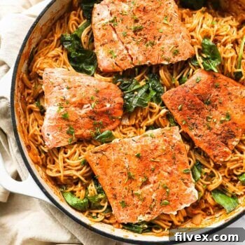 Close up overhead image of a skillet filled with pasta and four cajun salmon filets.