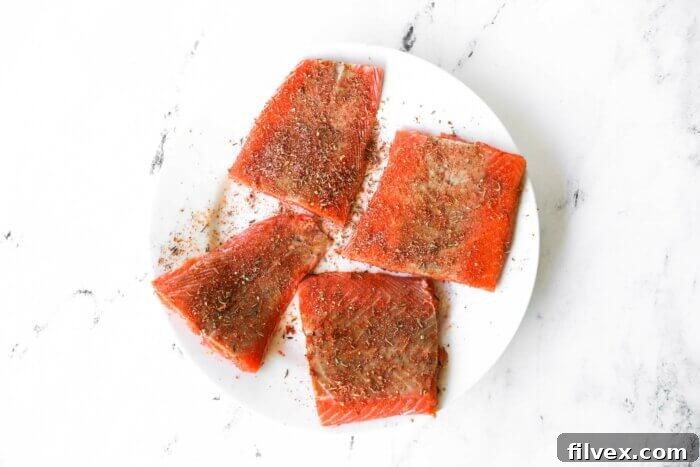 Four raw salmon filets on a plate covered in homemade cajun seasoning mix.