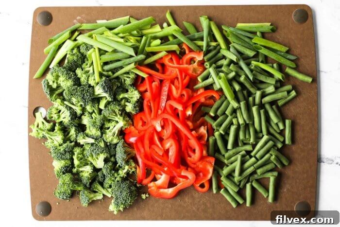 Prepped broccoli florets, green beans, red bell pepper and sliced onions on a cutting board