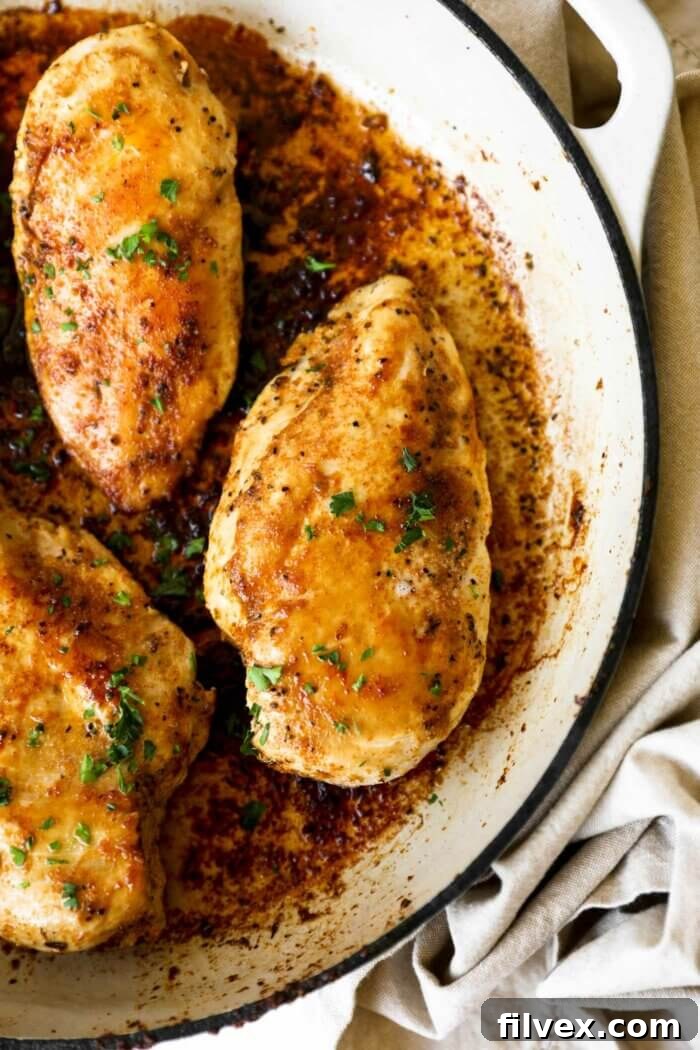 A beautifully cooked chicken breast in a cast iron skillet, glistening with butter and seasonings, ready to be served.