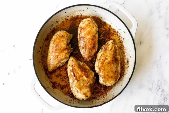 Horizontal image of four fully cooked, buttery chicken breasts in a skillet, garnished and ready for serving.