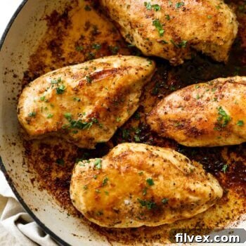Image of a cast iron skillet with four perfectly cooked chicken breasts in a rich, buttery sauce, garnished with fresh parsley.