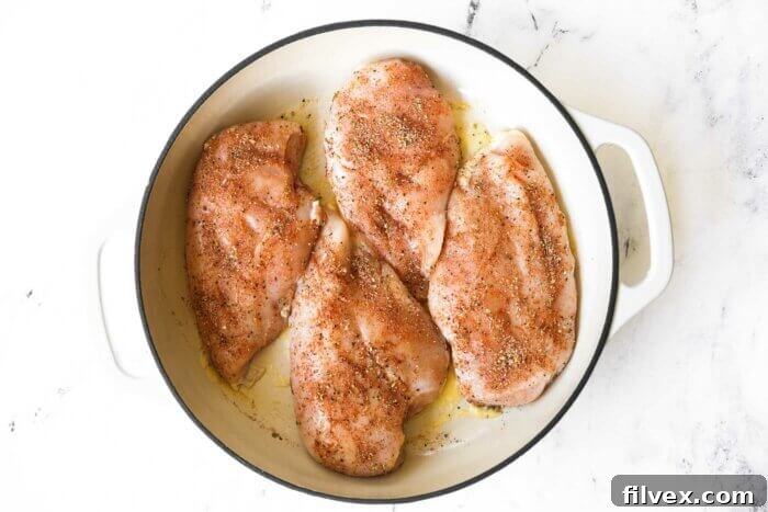 Four raw, seasoned chicken breasts carefully placed in a hot cast iron skillet with melted ghee, ready to begin searing.