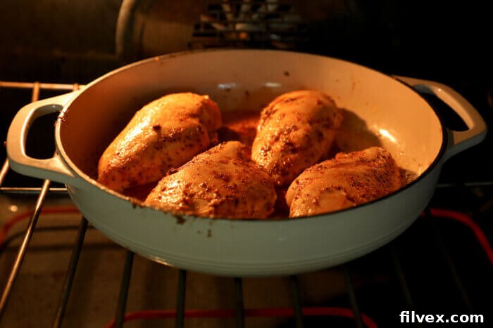 A cast iron skillet with four chicken breasts cooking inside an oven, capturing the roasting process.