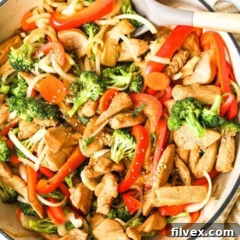 Marinated chicken stir fry with broccoli, onion and bell pepper in a skillet with spoon