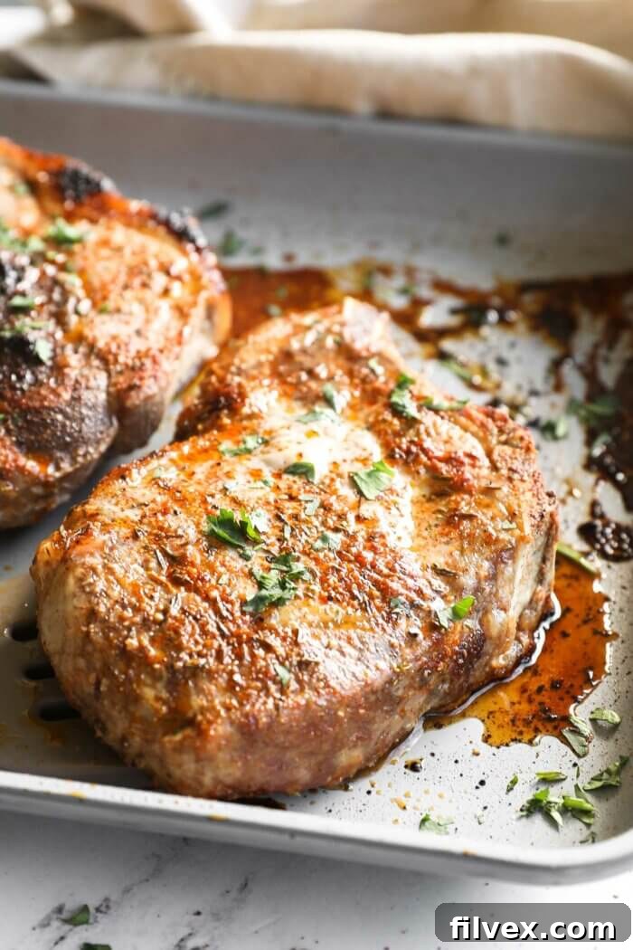 Beautifully seasoned raw bone-in pork chops on a baking sheet before cooking