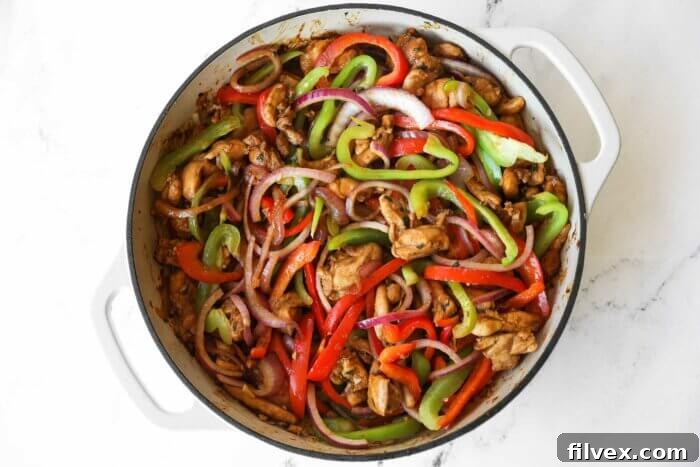 Chicken fajita ingredients (veggies + chicken) in a skillet cooking